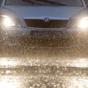 An image of a car driving in the rain with headlights on
