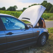 A photo of a car broken down on the side of the road with the bonnet up and a man looking at the engine